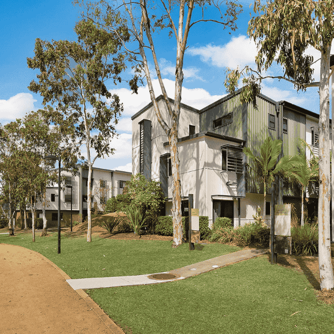Modern two-story residential buildings with white and gray facades surrounded by native trees and landscaped lawns.