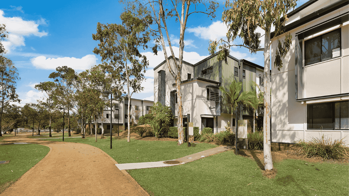 Modern two-story residential buildings with white and gray facades surrounded by native trees and landscaped lawns.