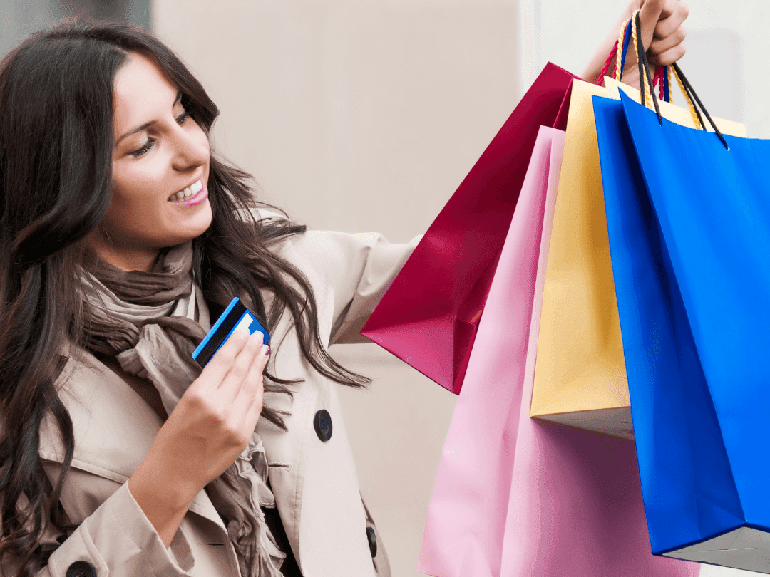 A woman smiling while holding shopping bags and a credit card near Acclaim Hotel Calgary