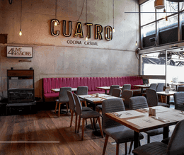 Illuminated Cuatro Cocina Casual sign above a long magenta banquet sofa with wooden tables at Hotel B3 Virrey