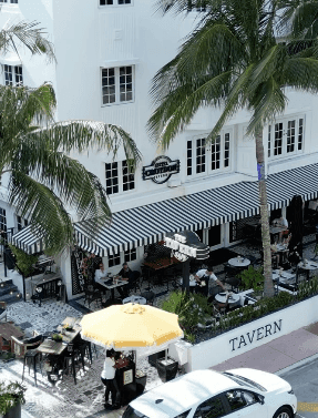 A white building with a black and white striped awning and a sign that says Tavern.