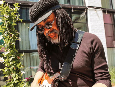 A man wearing a hat and glasses playing an electric guitar at The Verb Hotel