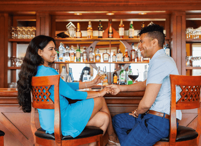 Couple enjoying wine while seated on wooden chairs by a fully stocked wooden bar at Rodd Crowbush Golf & Beach Resort