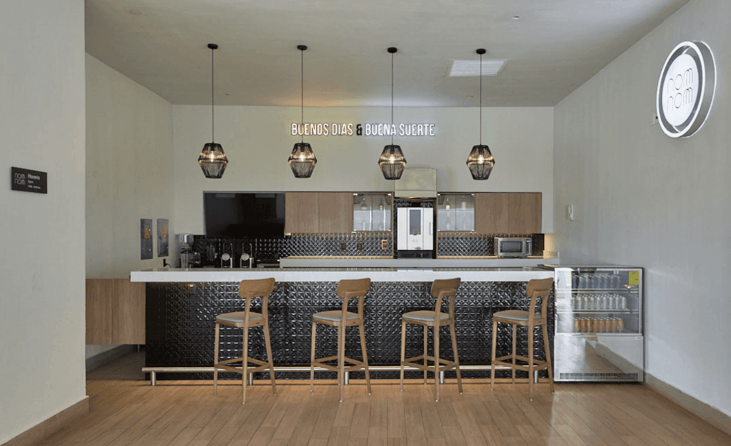 Cafetería del hotel con azulejos negros texturizados y letrero de neón que dice Buenos Días & Buena Suerte en Fiesta Inn