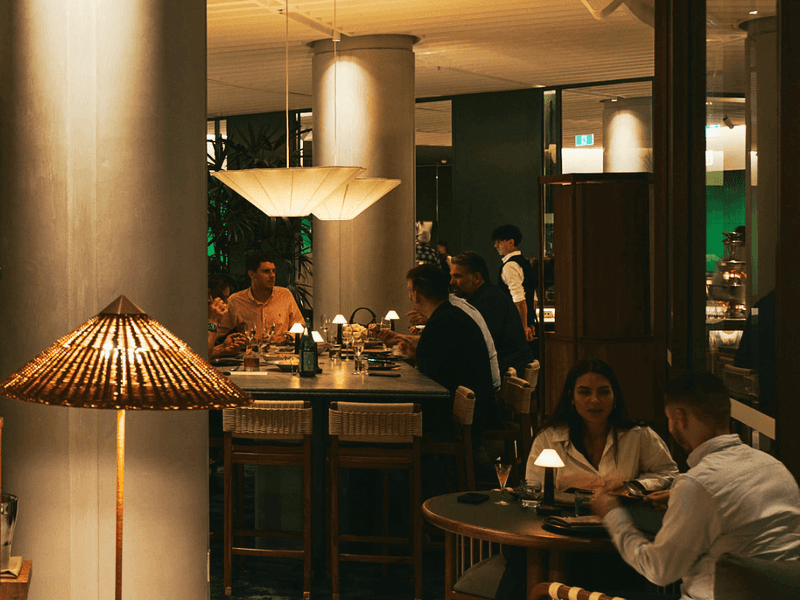 People seated at tables in a restaurant with large columns, decorative lighting, and a tiled floor.