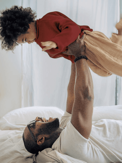 Adult holding a baby upside down playfully over a bed in a bright room at Sofitel Brisbane Central