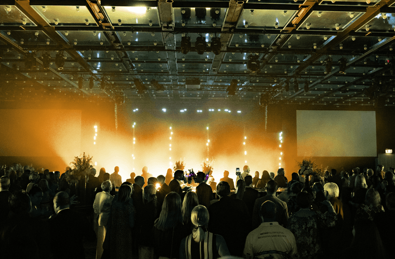 Large crowd at indoor concert or event with stage lighting and silhouetted audience