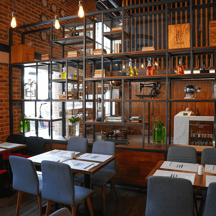 Mesas con sillas grises frente a estantería metálica negra con objetos antiguos en el restaurante de Unika Hotels