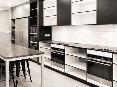 Modern shared kitchen with stainless steel appliances, white subway tile backsplash, and communal dining table at Student Living - Waymouth