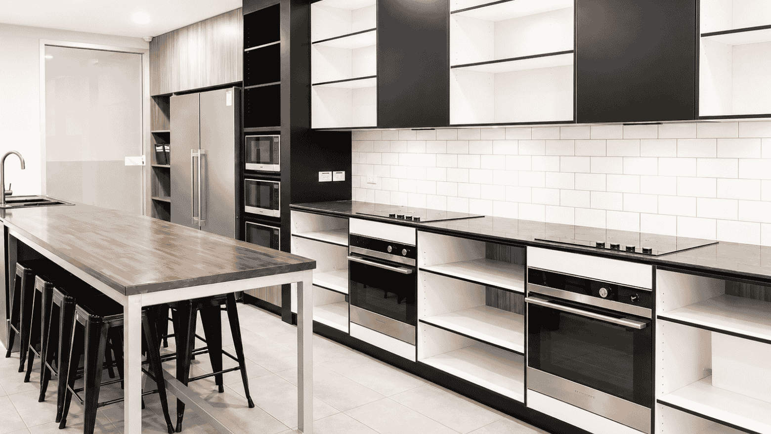 Modern shared kitchen with stainless steel appliances, white subway tile backsplash, and communal dining table at Student Living - Waymouth