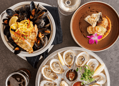 Mussels, oysters and scallops arranged on plates beside wine and beer on a table at Rodd Crowbush Golf & Beach Resort