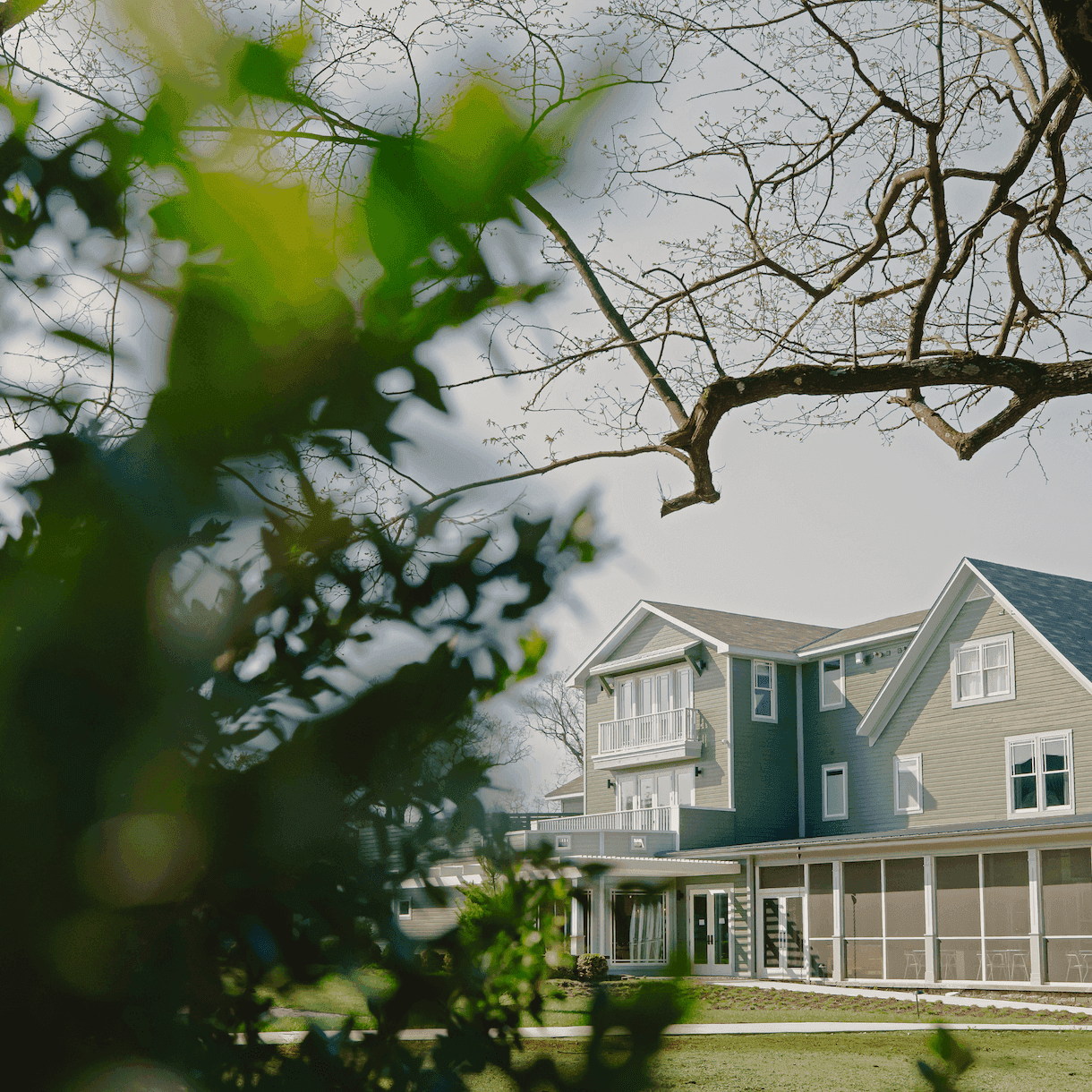 Exterior of the Stonebreaker hotel with a gray roof, white windows, and a screened porch, framed by trees.