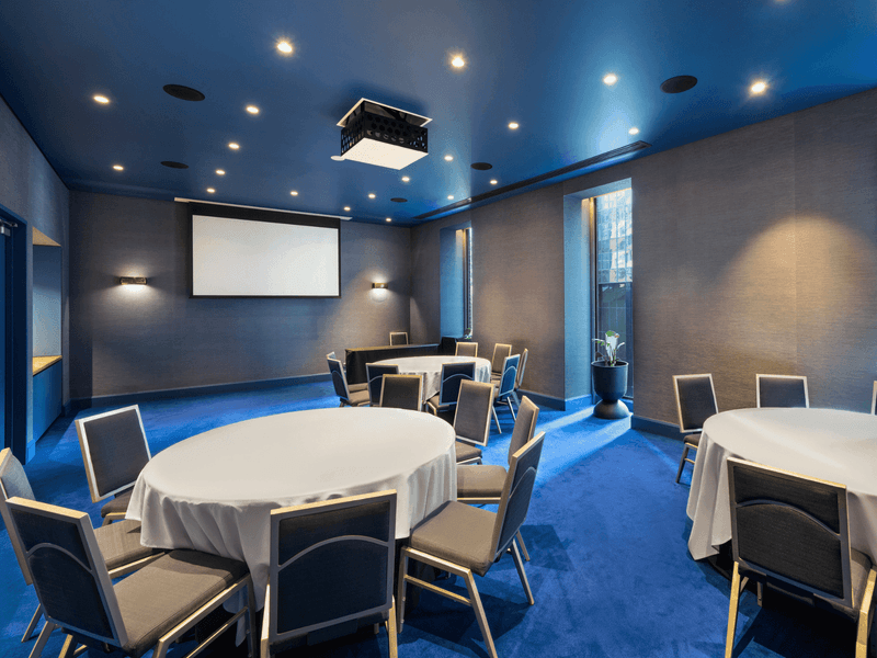 Edwin Flack room meeting space with round tables, presentation screen and modern blue ceiling