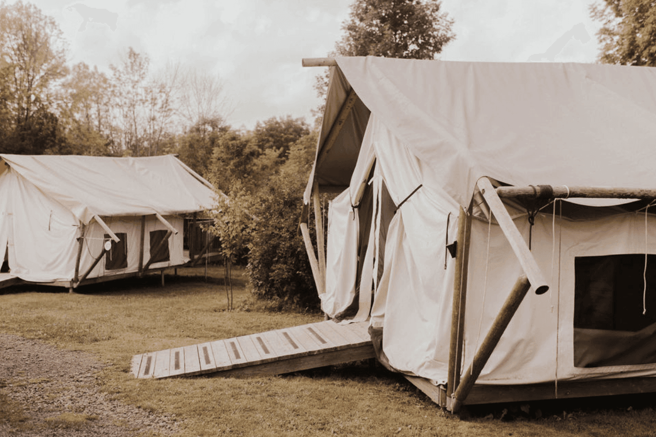 Two canvas glamping tents with wooden entry ramps set on grass beneath tall, shady trees at La Tourelle Inn and Spa