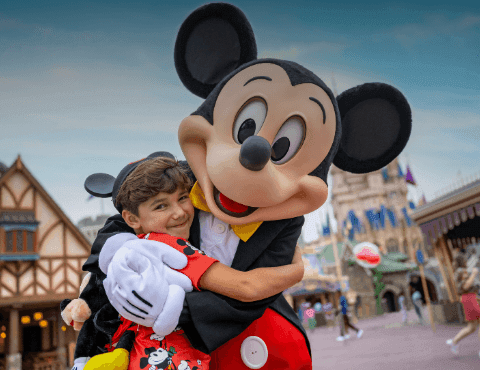 Mickey Mouse hugging a young boy in front of a fairytale castle at Walt Disney World Resort near Rosen Inn International