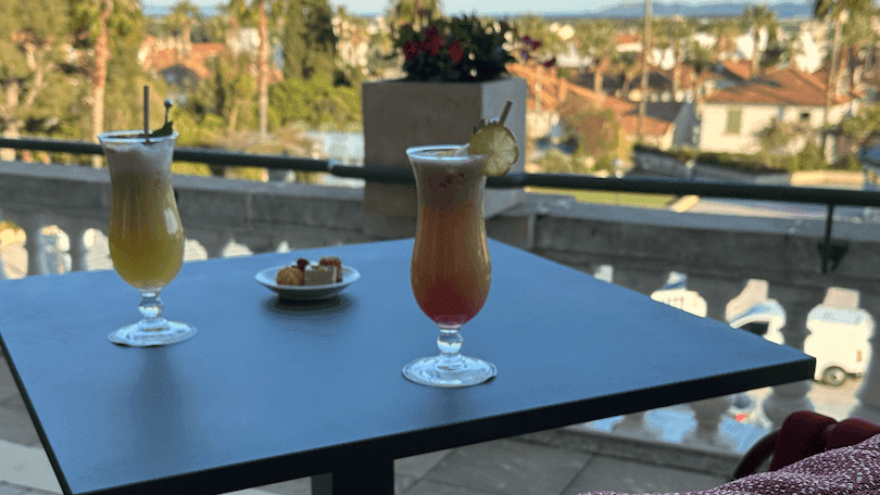Deux verres de cocktails sur une table en terrasse avec vue sur les palmiers et les maisons.