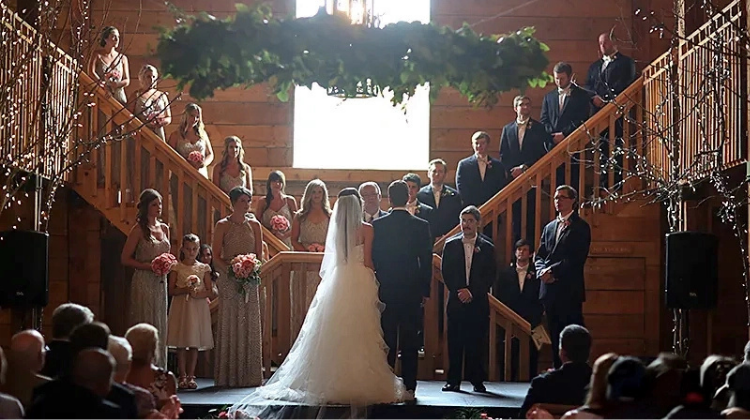 A bride and groom standing at the altar surrounded by loved ones in a rustic barn venue