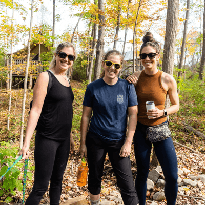 Three friends wearing sunglasses and activewear standing along wooded trail hike at La Tourelle Hotel and Spa