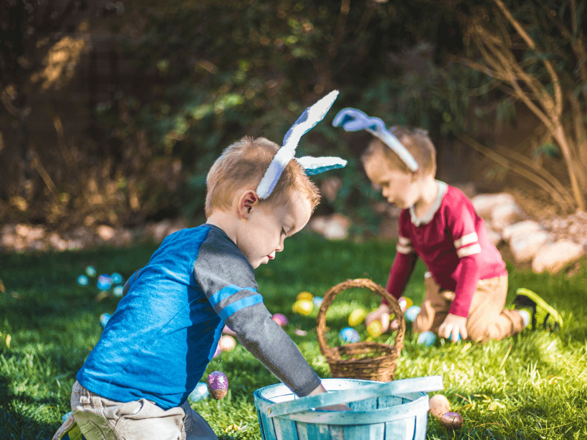 Două copii cu urechi de iepure caută ouă de Paște pe iarbă pentru Ofertă Family - Vacanța de Paște.