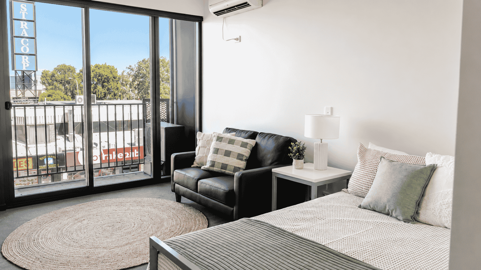 Modern studio apartment with bed, black leather sofa, and balcony access at Student Living - Waymouth