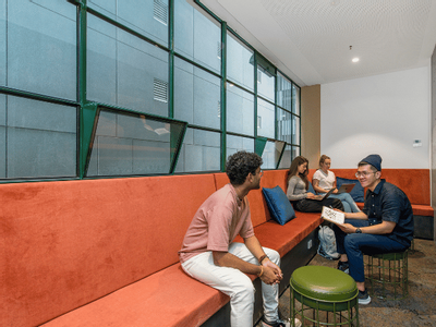 Group of people sit on red cushioned benches and stools in a modern study lounge.