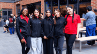 Five UniLodge staff members in branded uniforms smiling together at an outdoor courtyard event with brick building backdrop
