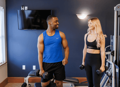 Couple holding dumbbells by a workout bench and weight machine in the fitness gym at Rodd Crowbush Golf & Beach Resort