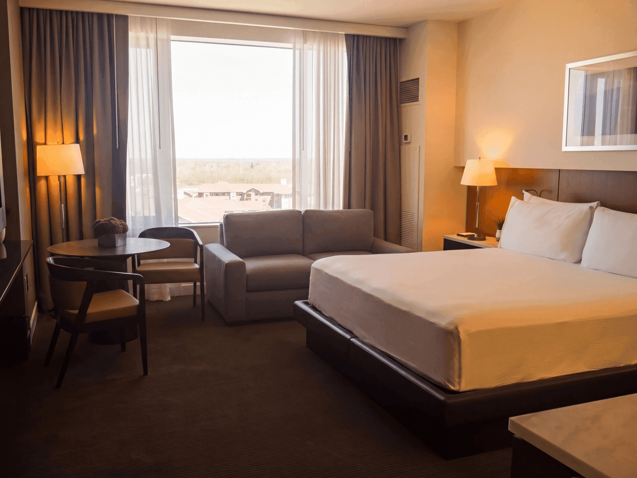 Gran Luxe King guestroom bedside detail with plush white bedding, warm wood headboard, reading light, and marble nightstand with lamp and clock.
