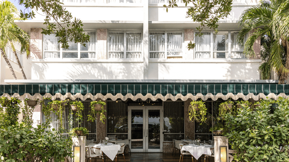 A restaurant exterior with outdoor seating, a green awning, and plants
