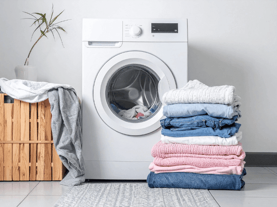 Neatly folded laundry beside a front-loading washing machine and wooden basket at YWCA Fort Canning