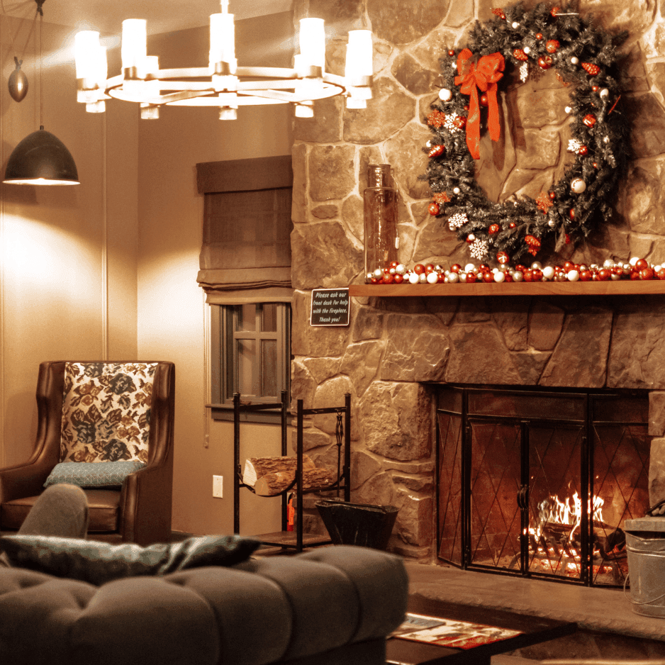 Christmas wreath and ornaments on a stone mantel above a lit fireplace by leather chairs at La Tourelle Inn and Spa