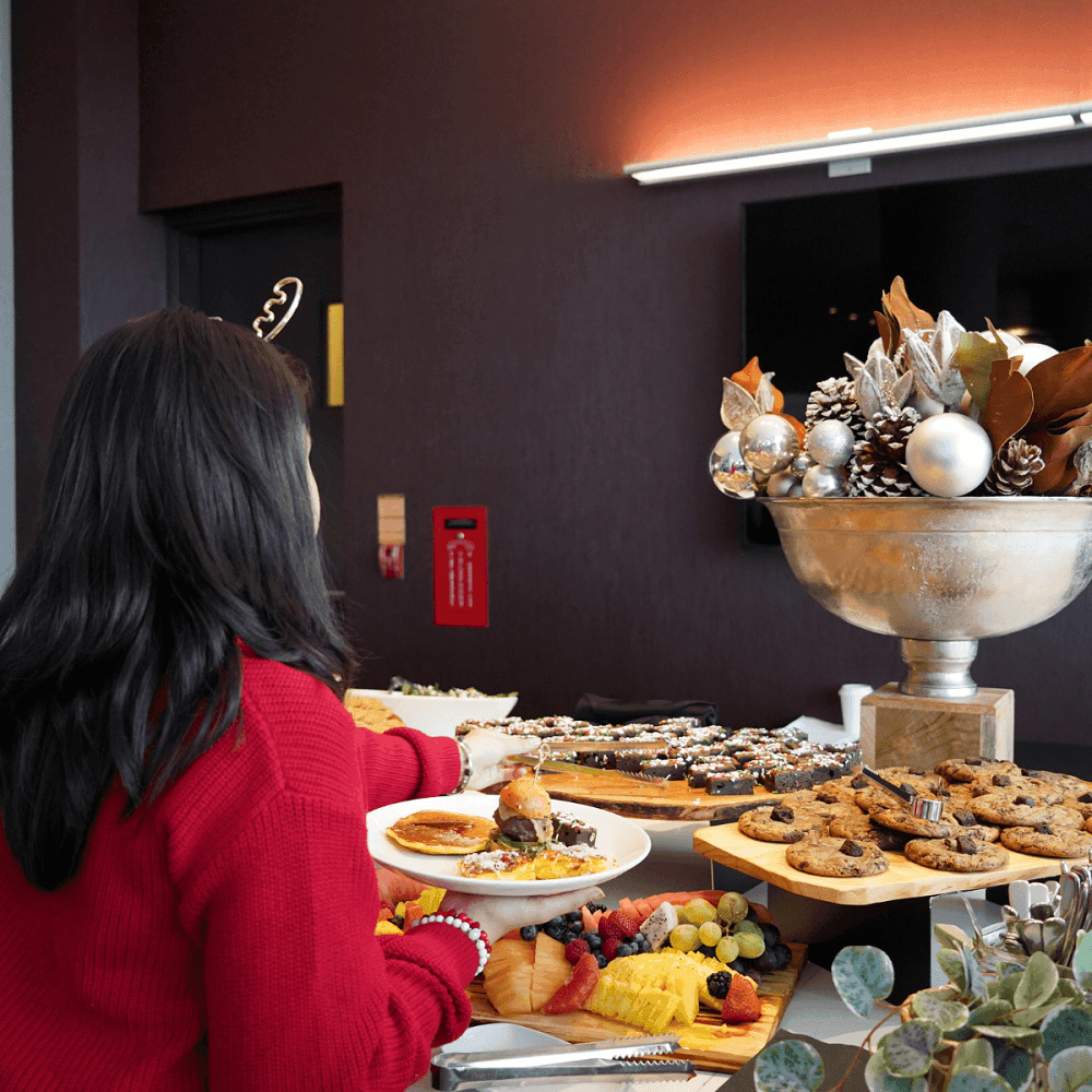Guest selecting cookies and fresh fruit from a festive buffet by a silver holiday ornament display at Hotel X Toronto