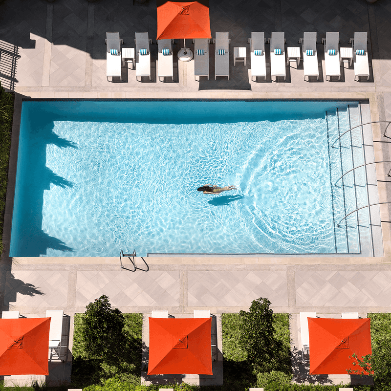 Aerial view of a swimming in a pool surrounded by lounge chairs and orange umbrellas at Warwick Hotels and Resorts