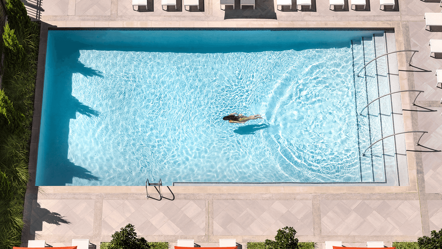 Aerial view of a swimming in a pool surrounded by lounge chairs and orange umbrellas at Warwick Hotels and Resorts