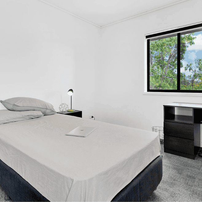 Modern bedroom with white walls, dark furniture, desk workspace, and window overlooking greenery at Springfield Central.