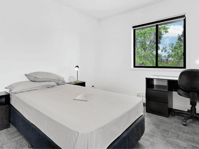 Modern bedroom with white walls, dark furniture, desk workspace, and window overlooking greenery at Springfield Central.