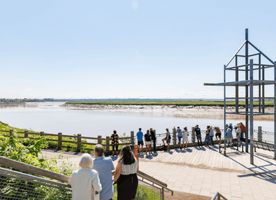 Crowd of people standing on a wooden riverside observation deck overlooking the Petitcodiac River near the Rodd Moncton