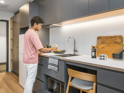 A man in a pink shirt stands at a kitchen counter preparing food near a sink.