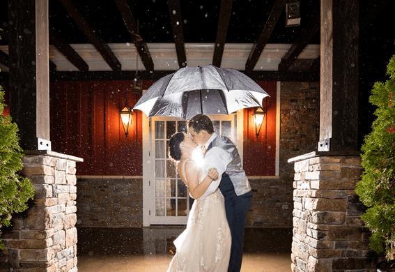 A wedded couple kissing under an umbrella by Inn at Willow Grove Virginia Resort