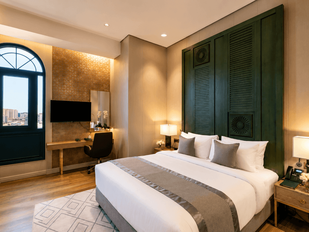 King bed beside arched window near desk with swivel office chair in Deluxe skyline view at Naviti by Warwick Jeddah