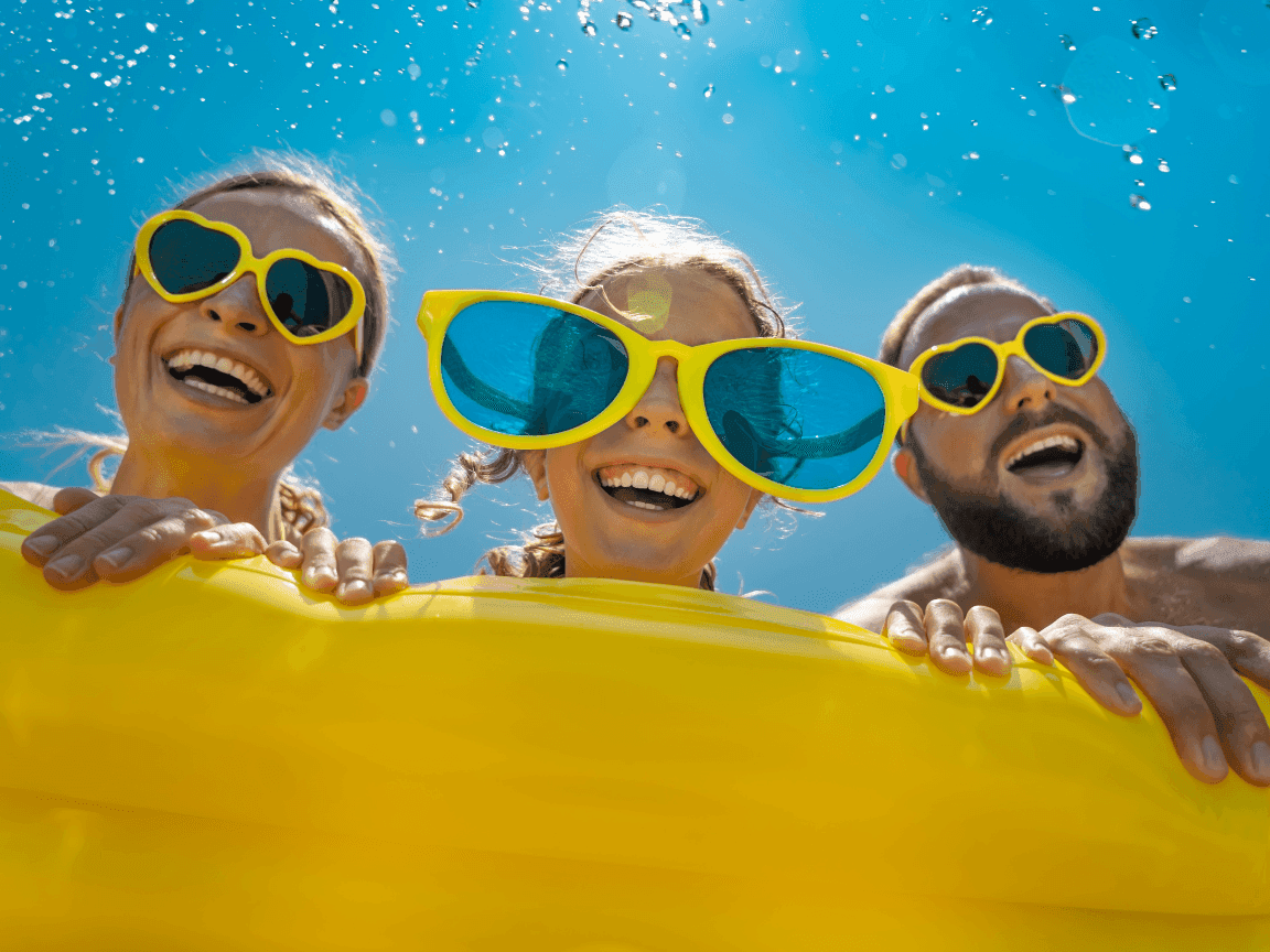 Three people posing with sunglasses in a pool at Amora Hotel