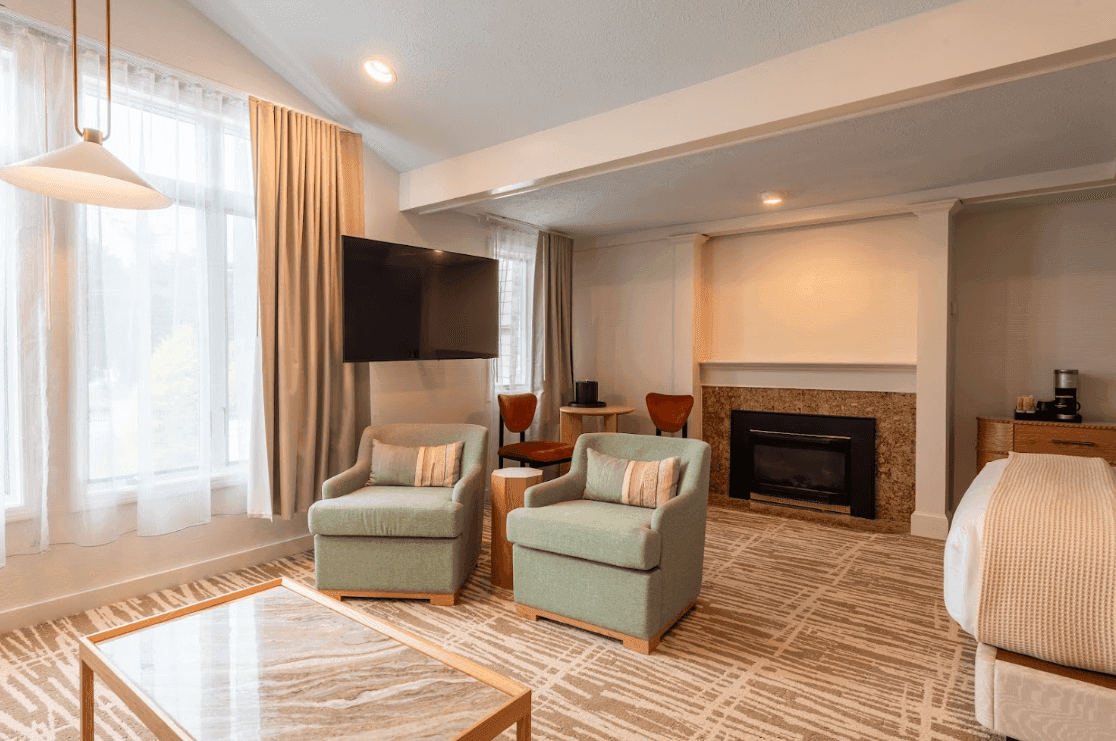 A spacious hotel room with a fireplace, large window, and modern decor.
