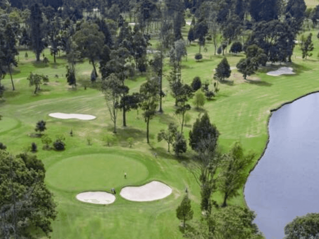 Campo de golf exuberante con un green impecablemente cuidado, varios búnkers de arena y un lago sereno que bordea el fairway bajo un cielo despejado