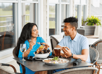Couple enjoying fresh seafood at a table by large windows overlooking greenery at Rodd Crowbush Golf & Beach Resort