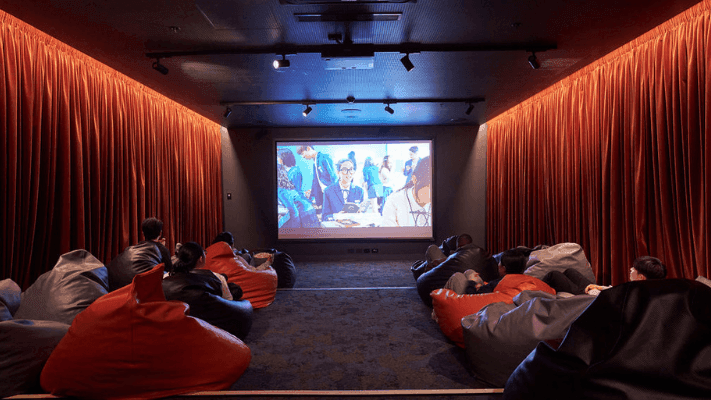 People sitting in beanbag chairs watching a movie projected on a screen in a theater.