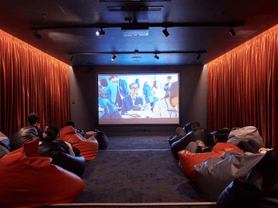 People sitting in beanbag chairs watching a movie projected on a screen in a theater.