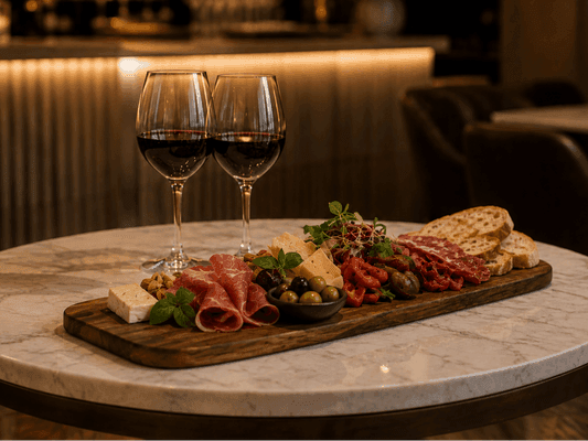 Charcuterie board with cured meats, cheese, olives, antipasto and crusty bread served on a marble table with two glasses of red wine in a hotel restaurant.