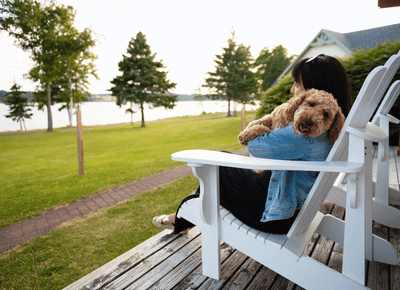 Woman holding a golden doodle dog while relaxing in a white Adirondack chair on a wooden deck patio at Rodd Hotels & Resorts