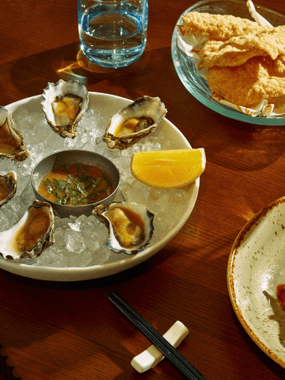 Plates of oysters, fried fish, and seafood with a wine glass on a wooden table for Easter Seafood Banquet at Delta Rue.
