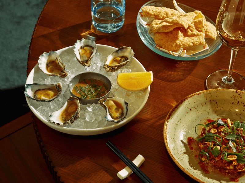 Plates of oysters, fried fish, and seafood with a wine glass on a wooden table for Easter Seafood Banquet at Delta Rue.